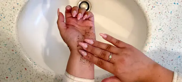 Mani con scrub per capire come togliere l'autoabbronzante. Unghie rosa e anello con cuore.