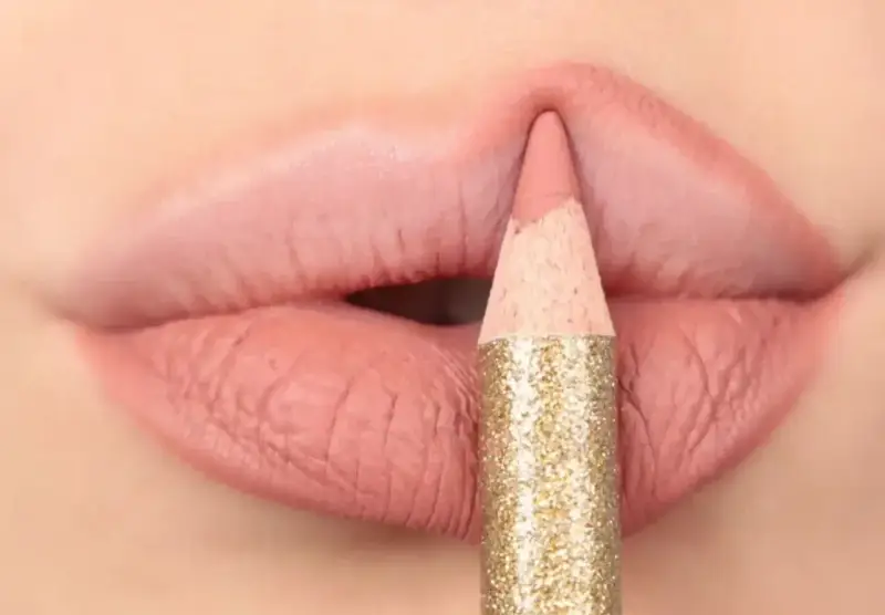 Matita glitterata color oro definisce il contorno delle labbra con un tratto preciso, creando un effetto overline labbra impeccabile.